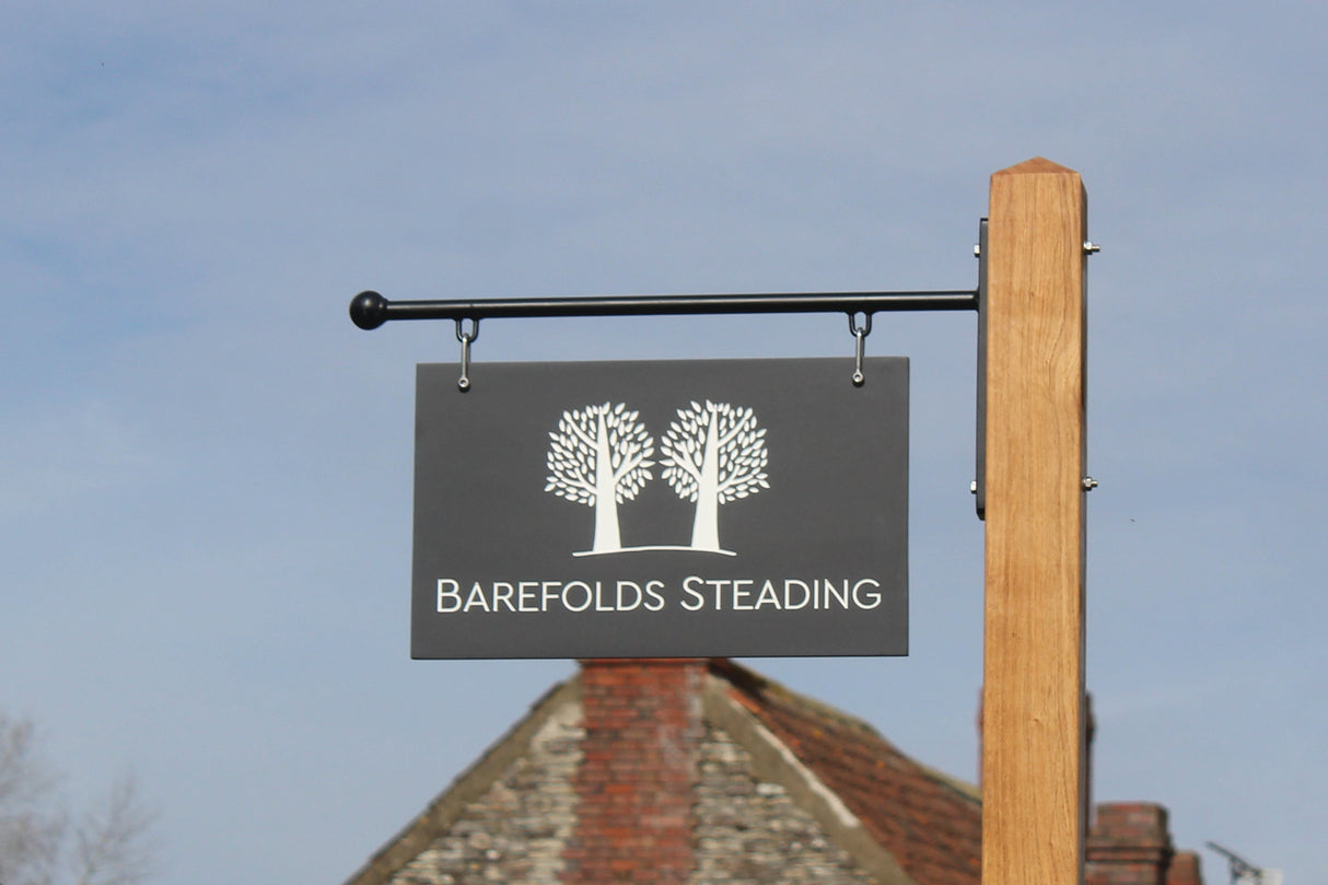 Corian Hanging Sign against a blue sky. Oak post and metal bracket