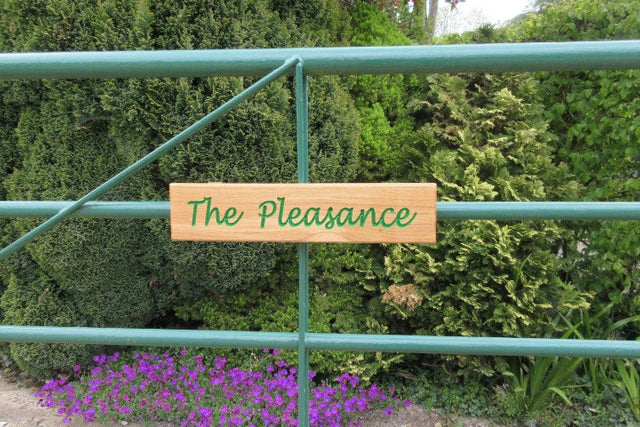 Green metal gate with a wooden sign reading 'The Pleasance' 